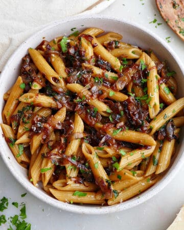 square image of caramelized shallot pasta in a serving bowl topped with chopped parsley