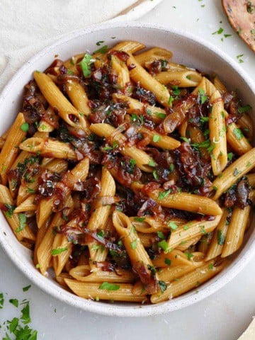 square image of caramelized shallot pasta in a serving bowl topped with chopped parsley