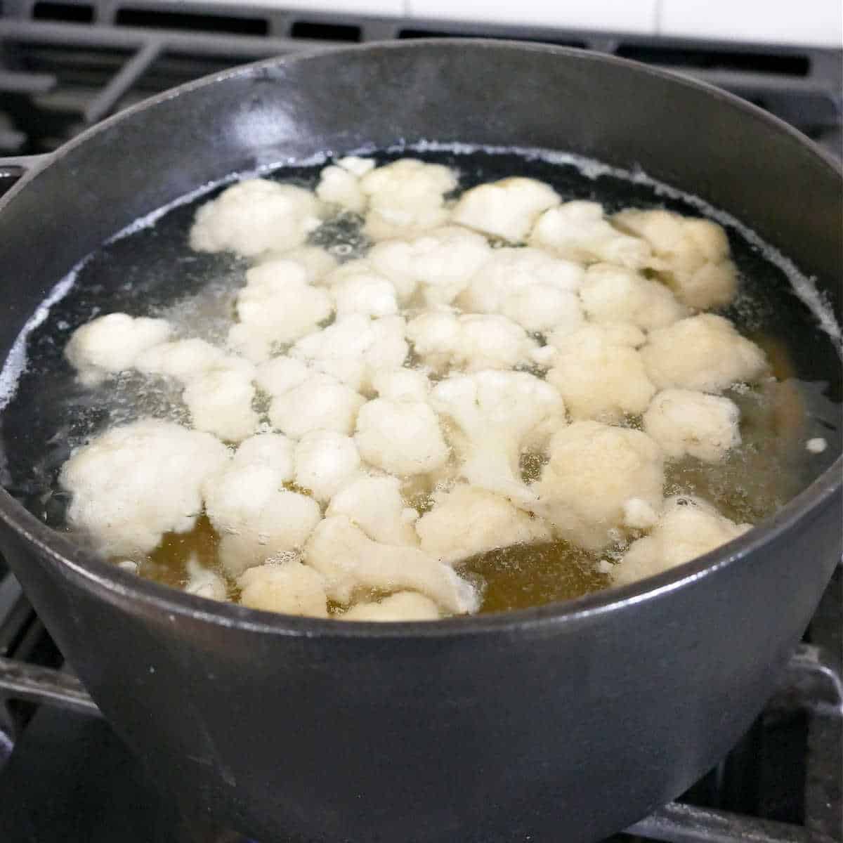 cauliflower and potatoes cooking in boiling water in a pot on the stove