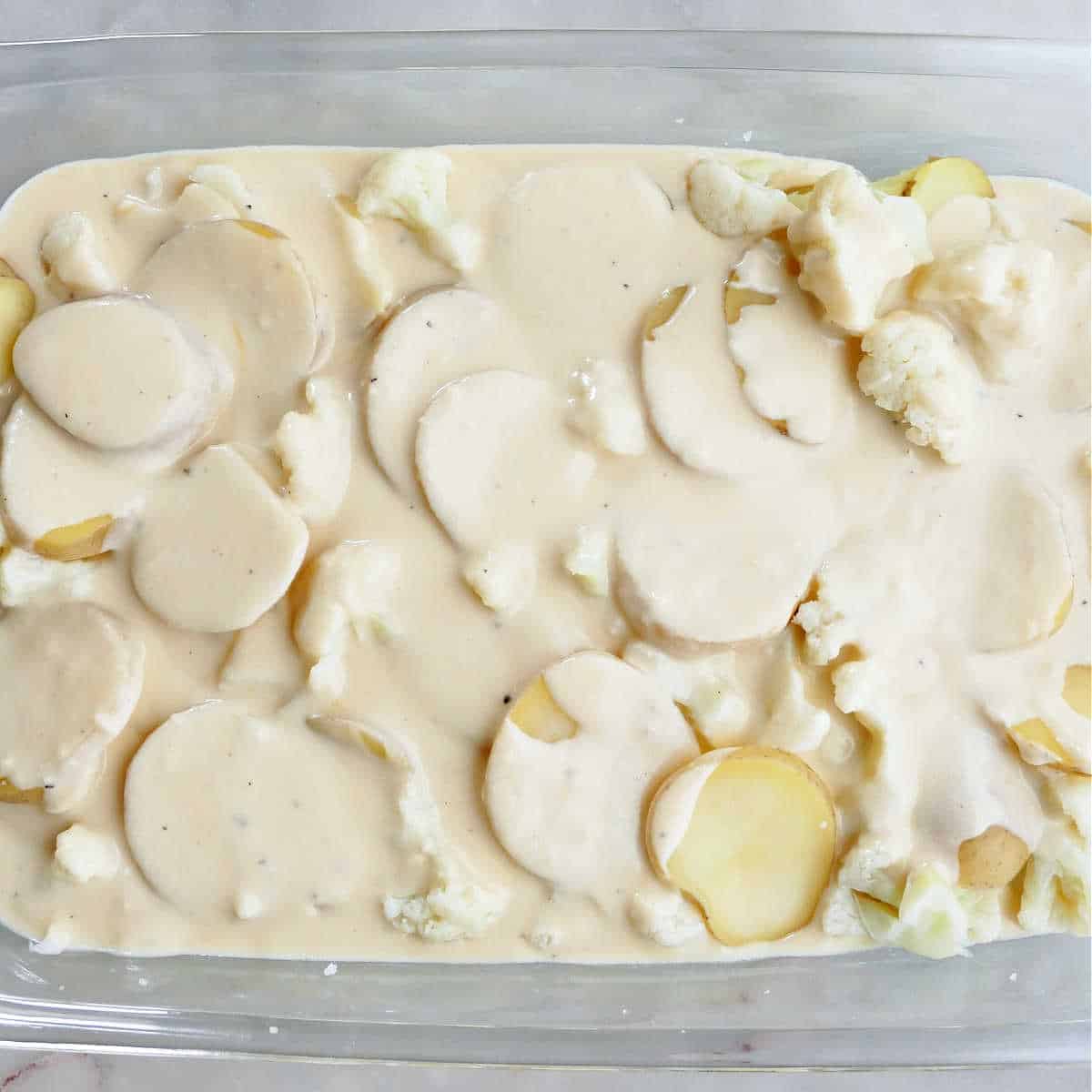 cauliflower and potatoes covered with a creamy sauce in a casserole dish