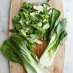 chopped bok choy and bok choy leaves on a bamboo cutting board on a counter