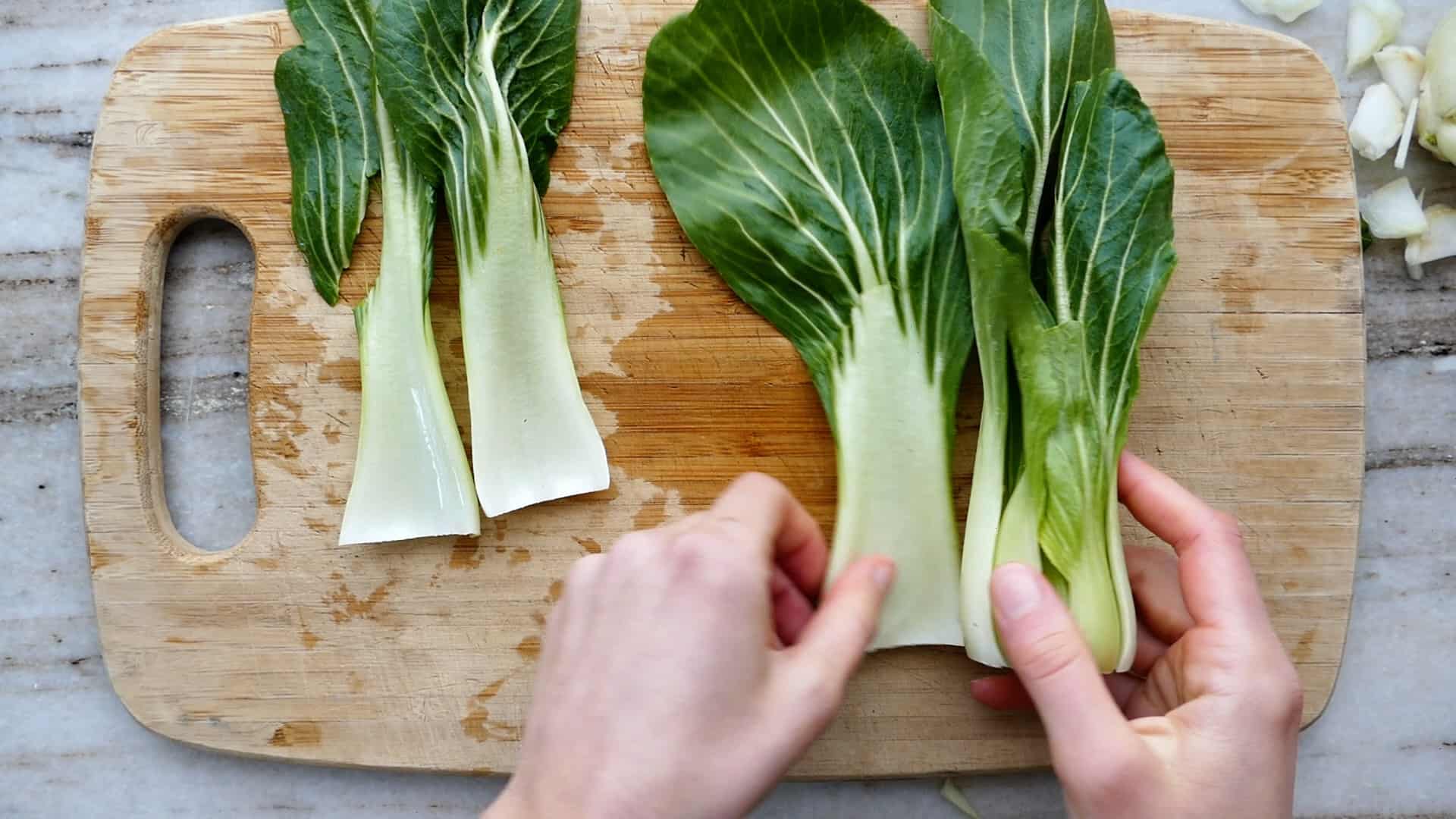 woman pulling apart the leaves of a head of bok choy over a cutting board