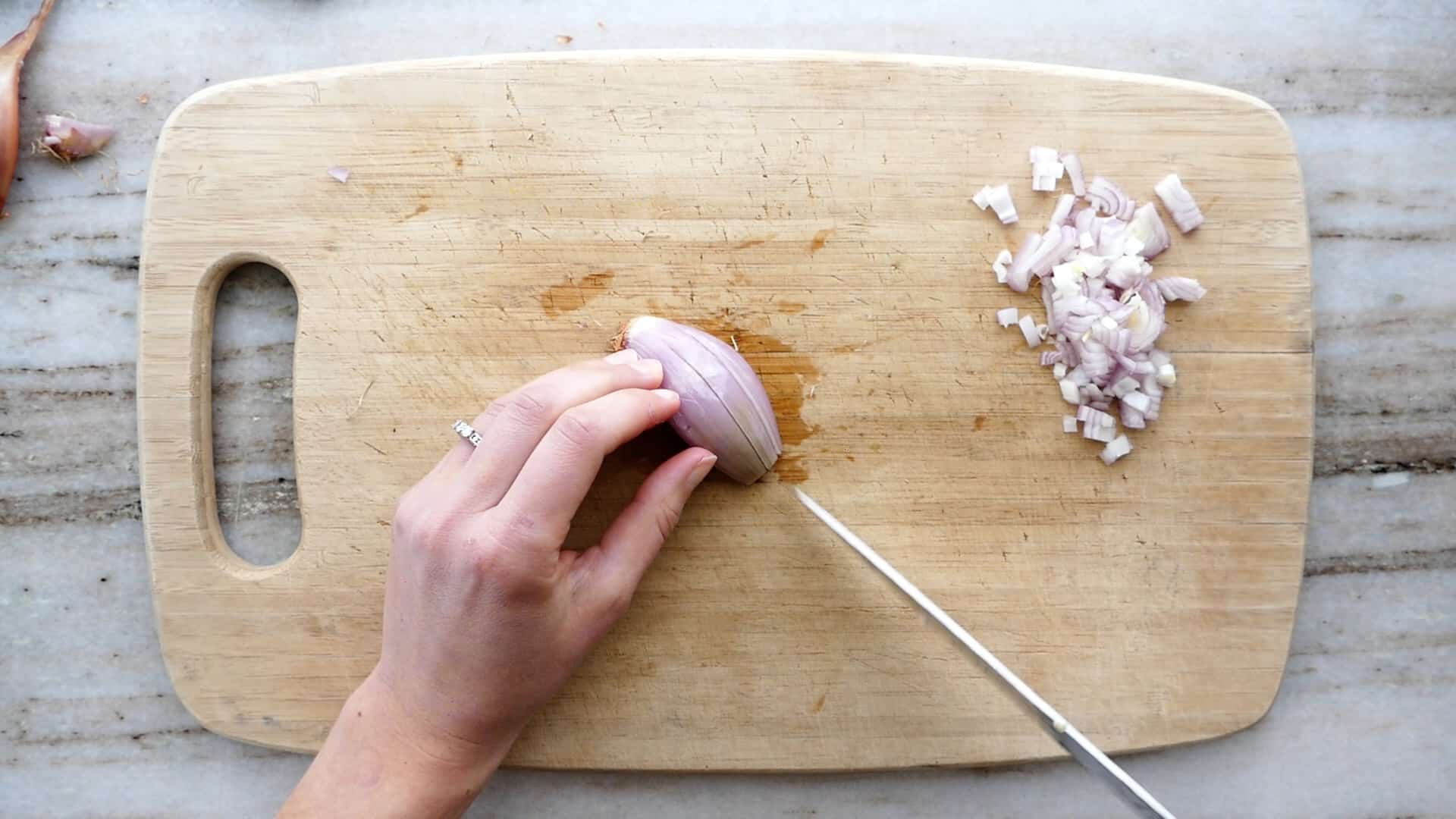 woman making lengthwise slits in half of a shallot on a bamboo cutting board