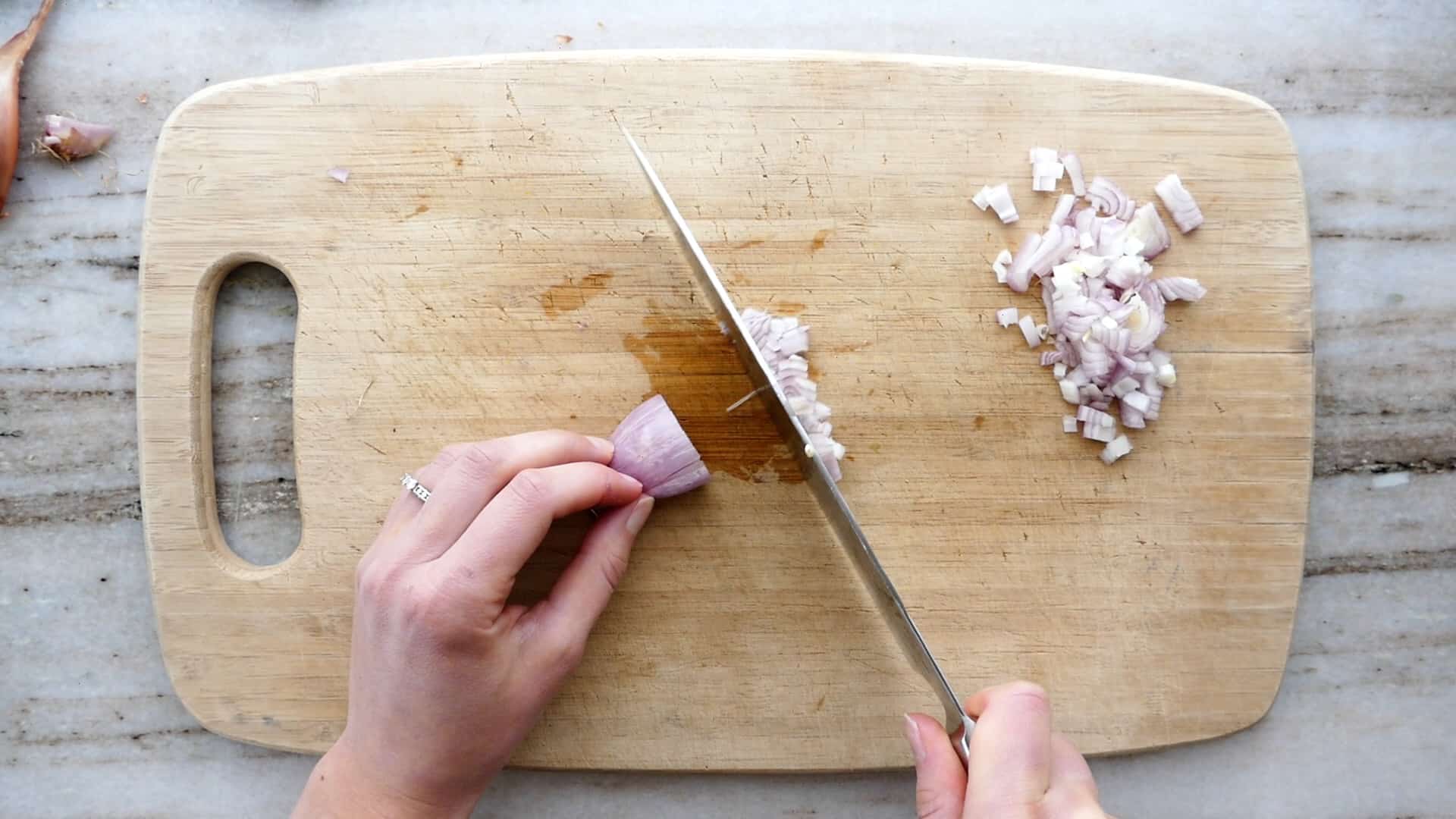 woman dicing a shallot with a knife on a bamboo cutting board