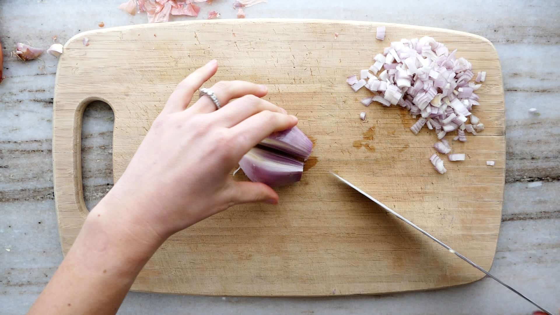 woman cutting a shallot in half lengthwise on a bamboo cutting board