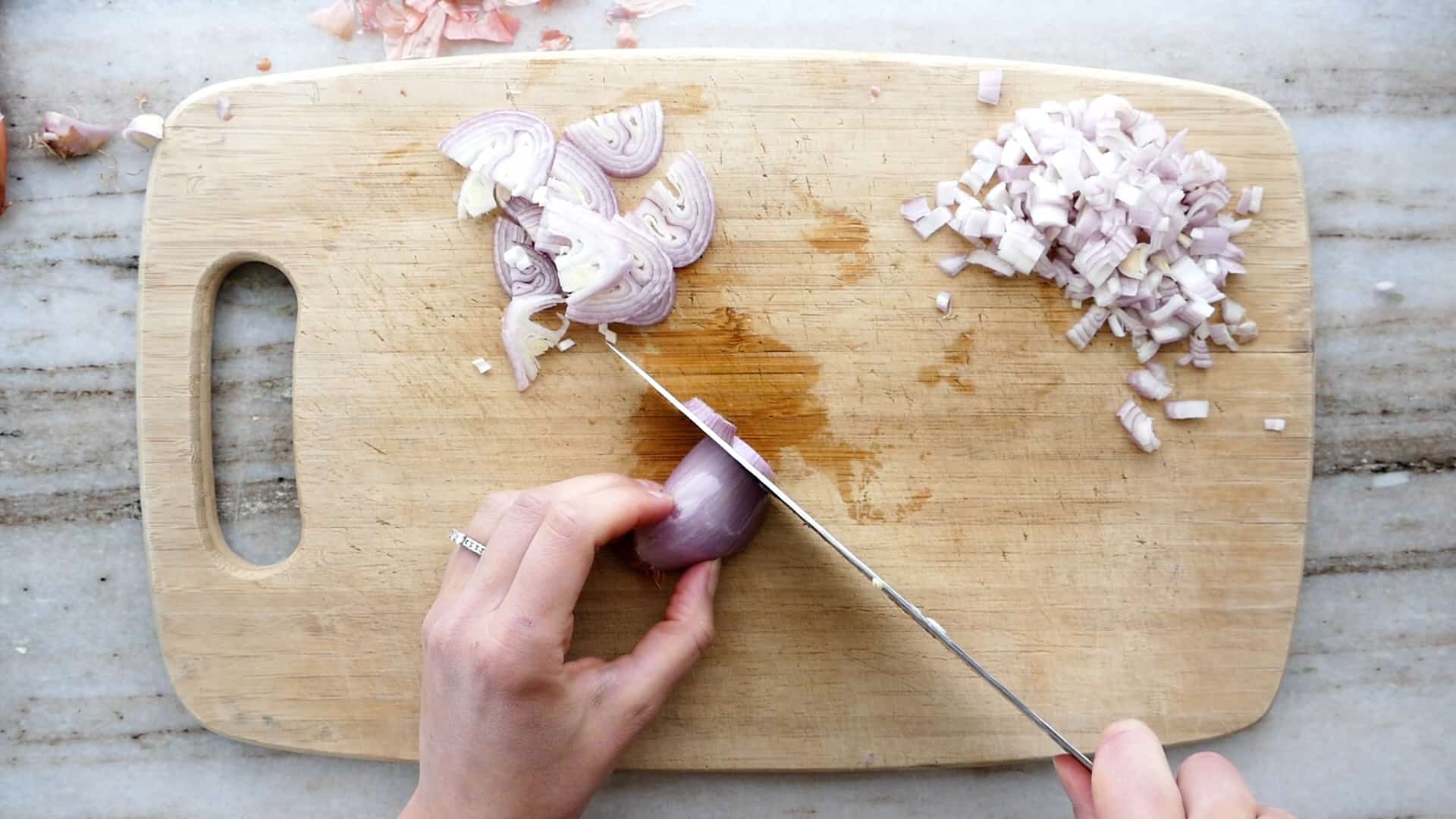 woman cutting a shallot into half rings on a bamboo cutting board