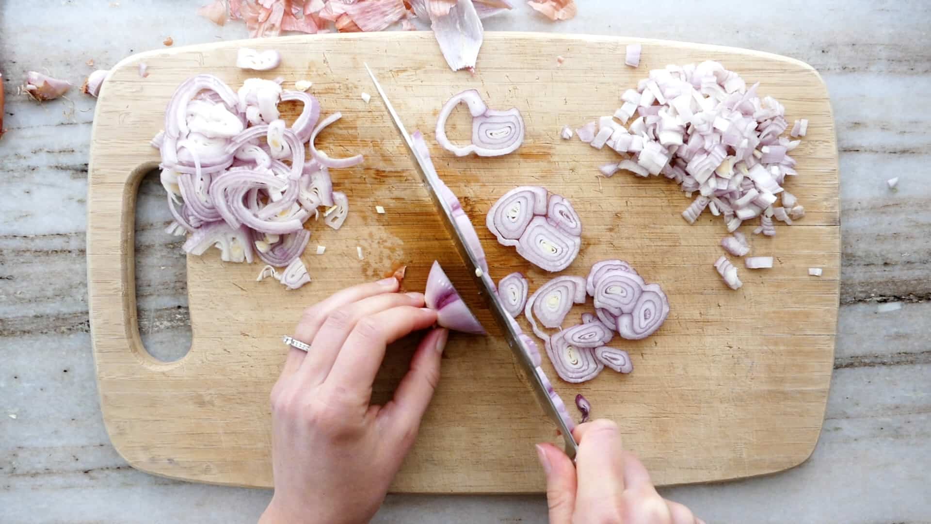 woman using a knife to cut scallions into slices on a bamboo cutting board