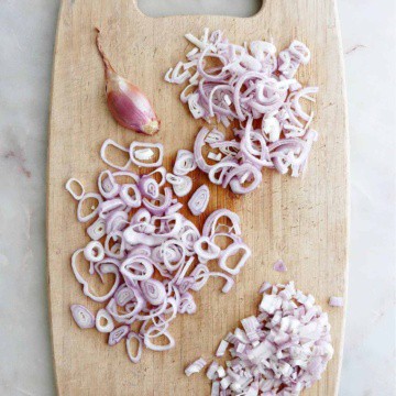 shallots cut in three different ways spread out next to each other on a bamboo cutting board