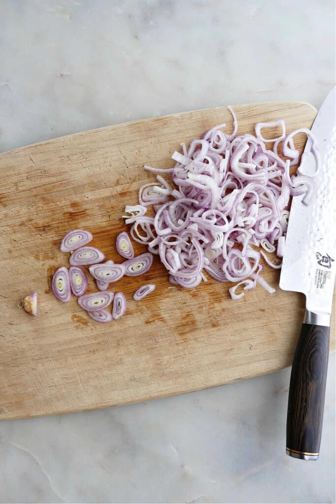 sliced shallots on a bamboo cutting board next to a chef's knife