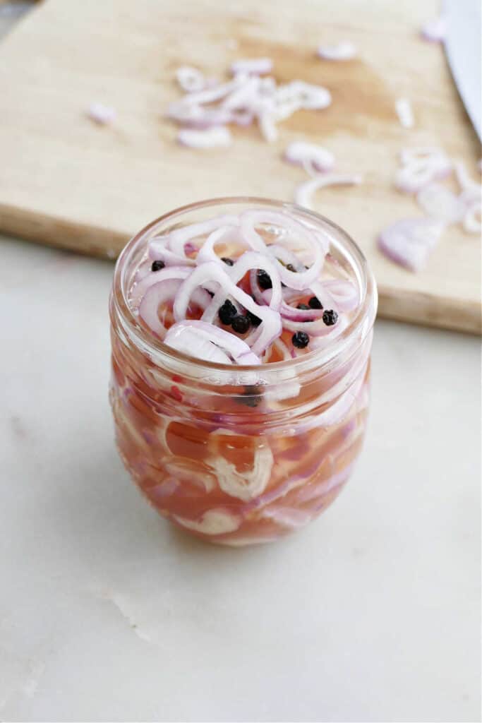 sliced shallots in a jar with vinegar and spices on a counter