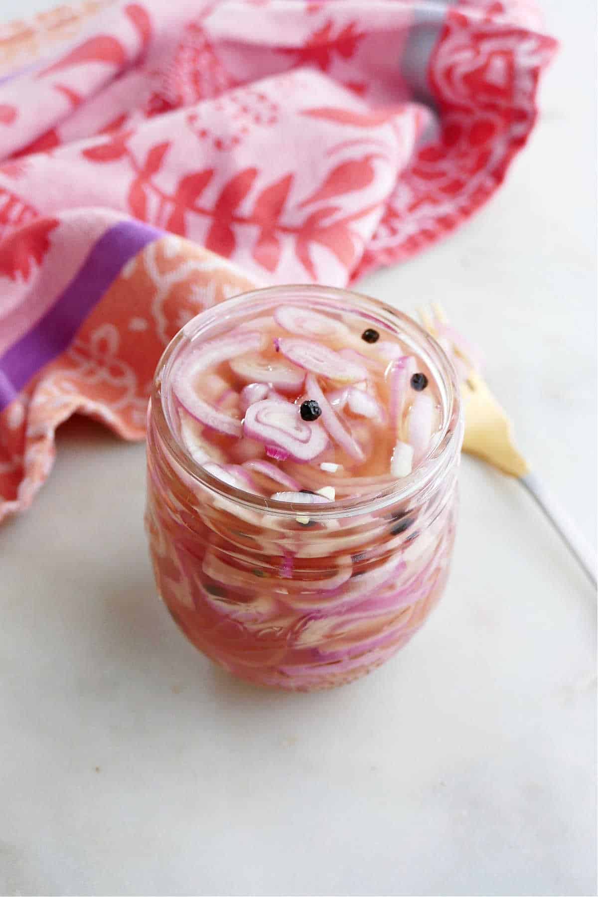 pickled shallots in a jar in front of a fork and towel