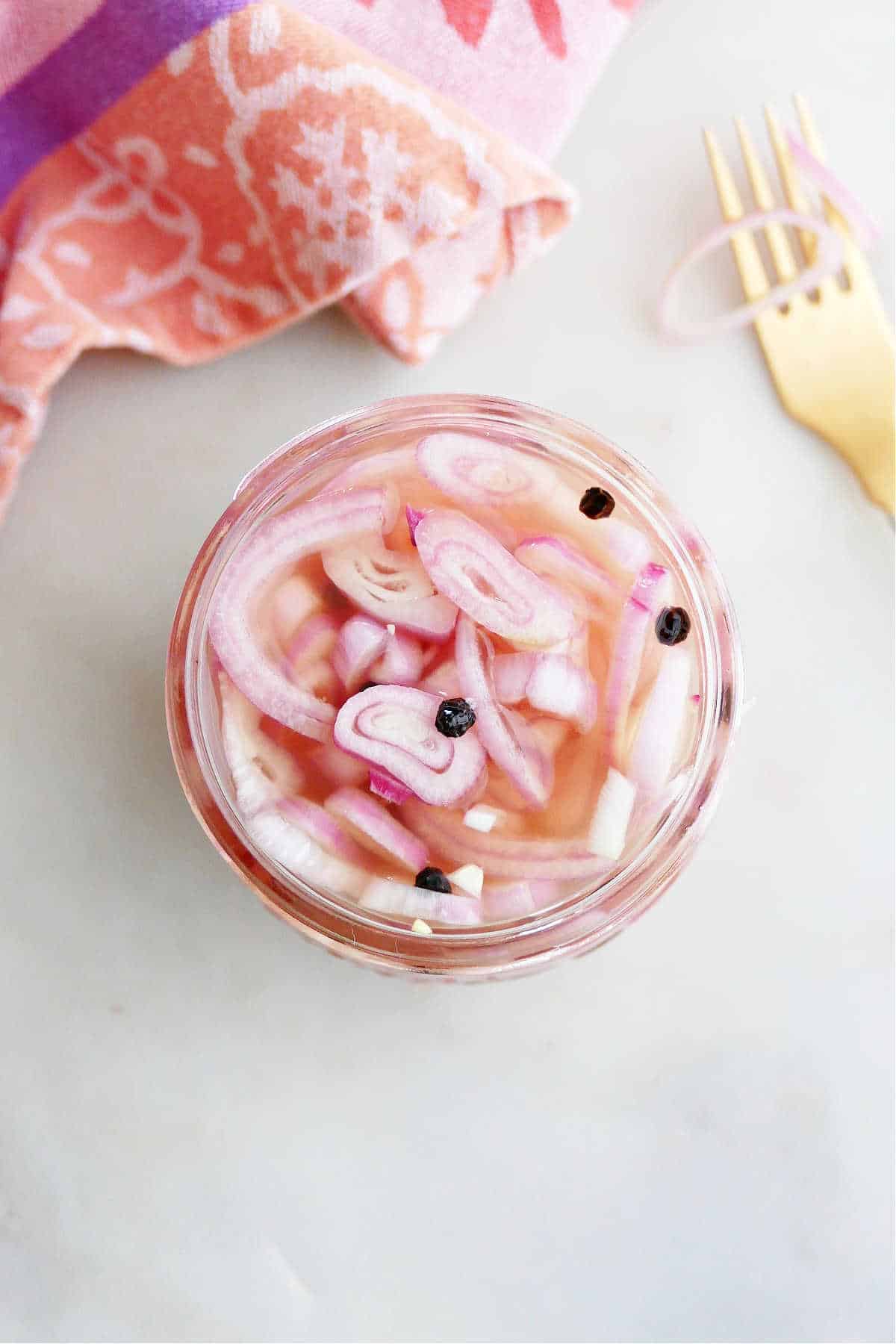 overhead photo of pickled shallots in a glass jar with brine and peppercorns