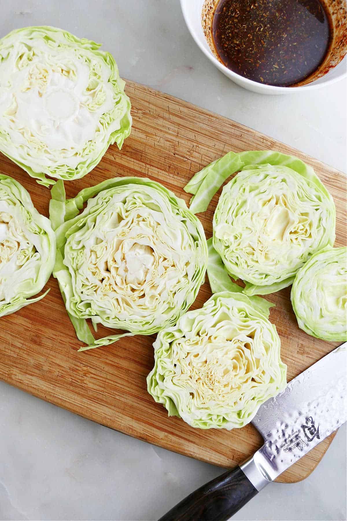 sliced cabbage steaks on a cutting board next to a knife and bowl with seasonings