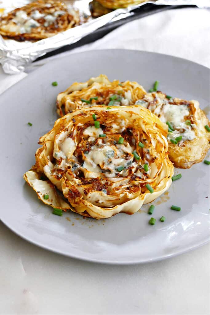 side view of roasted cabbage steaks topped with chives on a serving plate