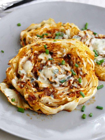 square image of side view of roasted cabbage steaks topped with chives on a serving plate
