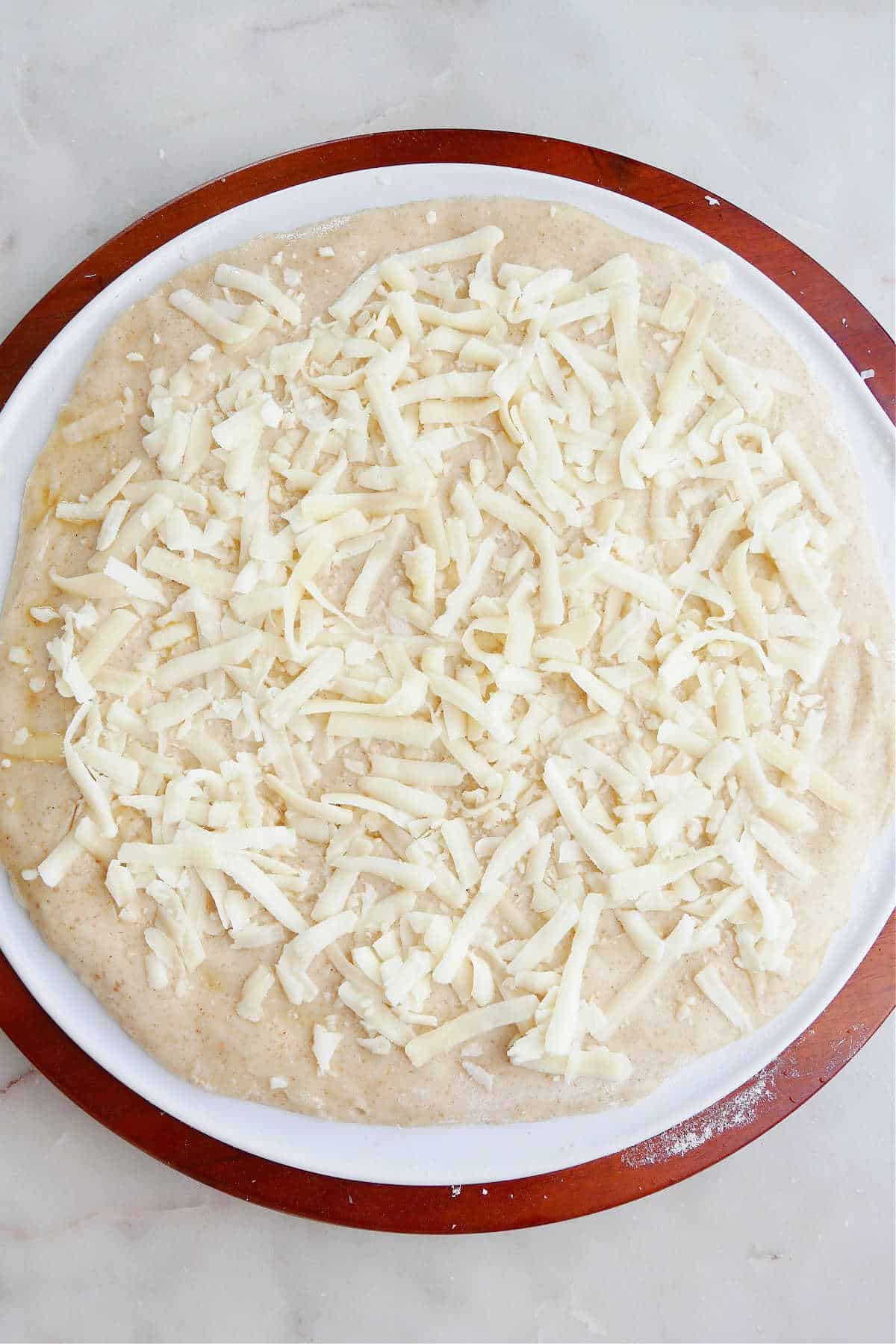 pizza dough on a pizza stone topped with mozzarella cheese