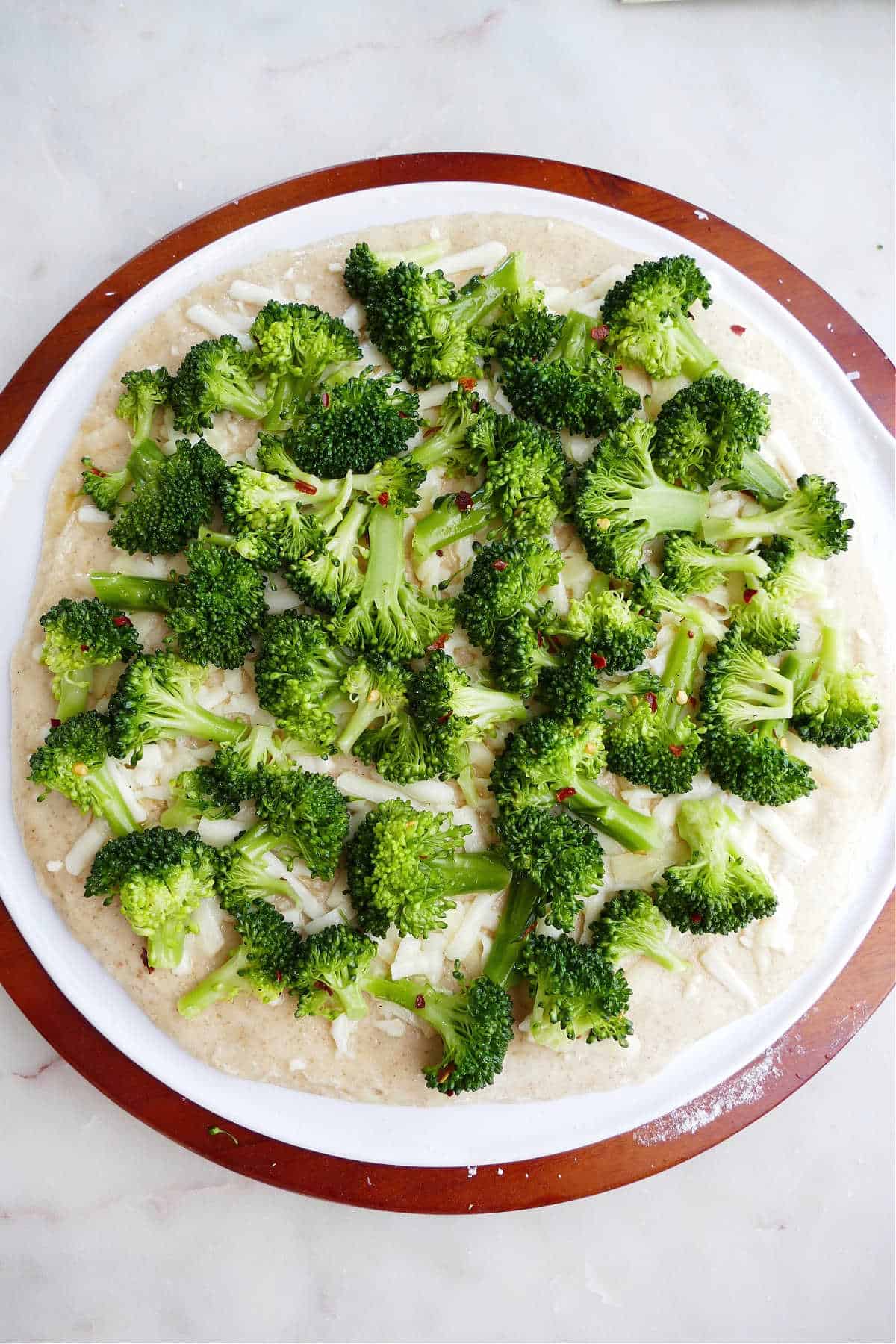 pizza dough on a pizza stone topped with cheese and broccoli