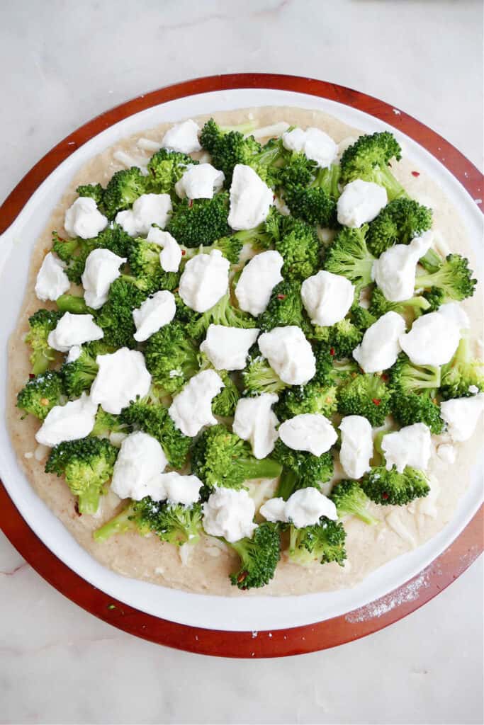 pizza dough on a pizza stone topped with cheese and broccoli