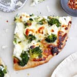 slice of white pizza with broccoli on a counter next to pizza slicer