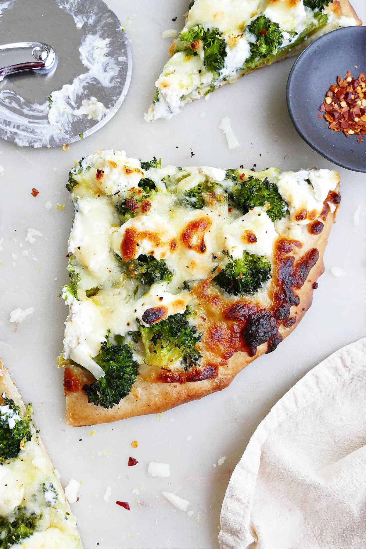 slice of white pizza with broccoli on a counter next to pizza slicer