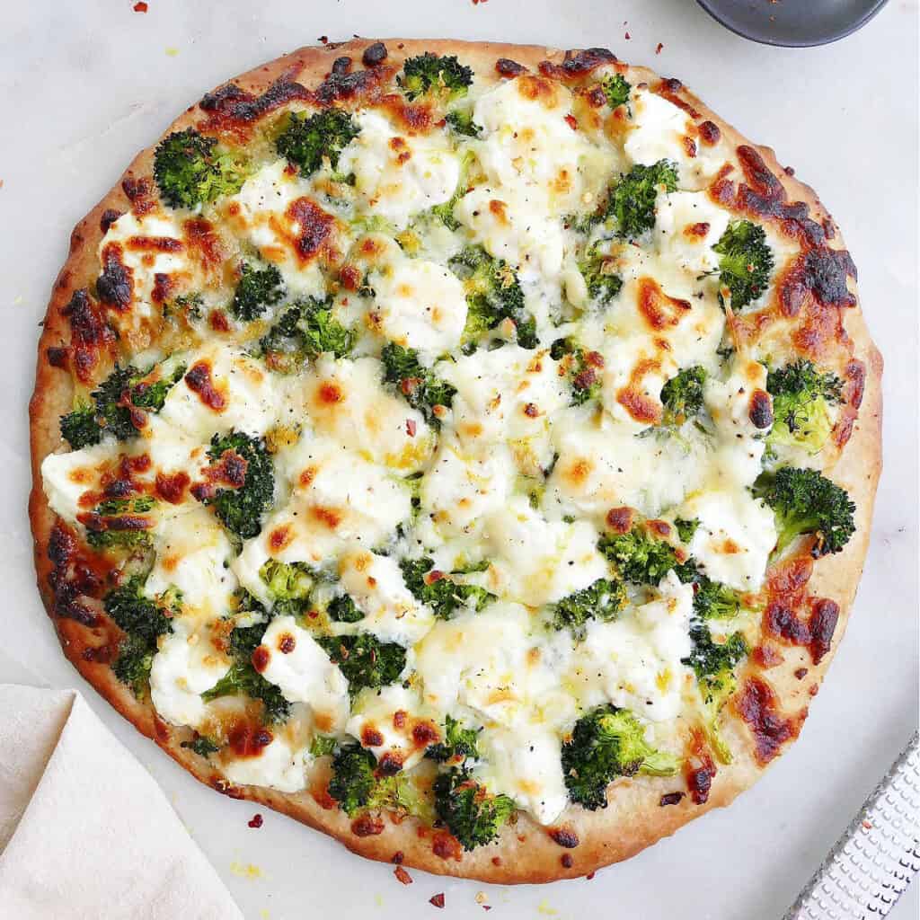 square image of white pizza with broccoli on a counter