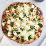 square image of white pizza with broccoli on a counter