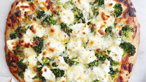 square image of white pizza with broccoli on a counter
