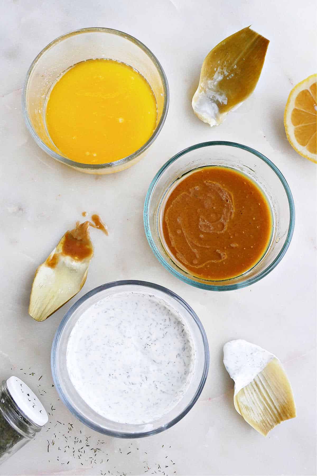 three artichoke dipping sauces in glass containers next to each other on a counter