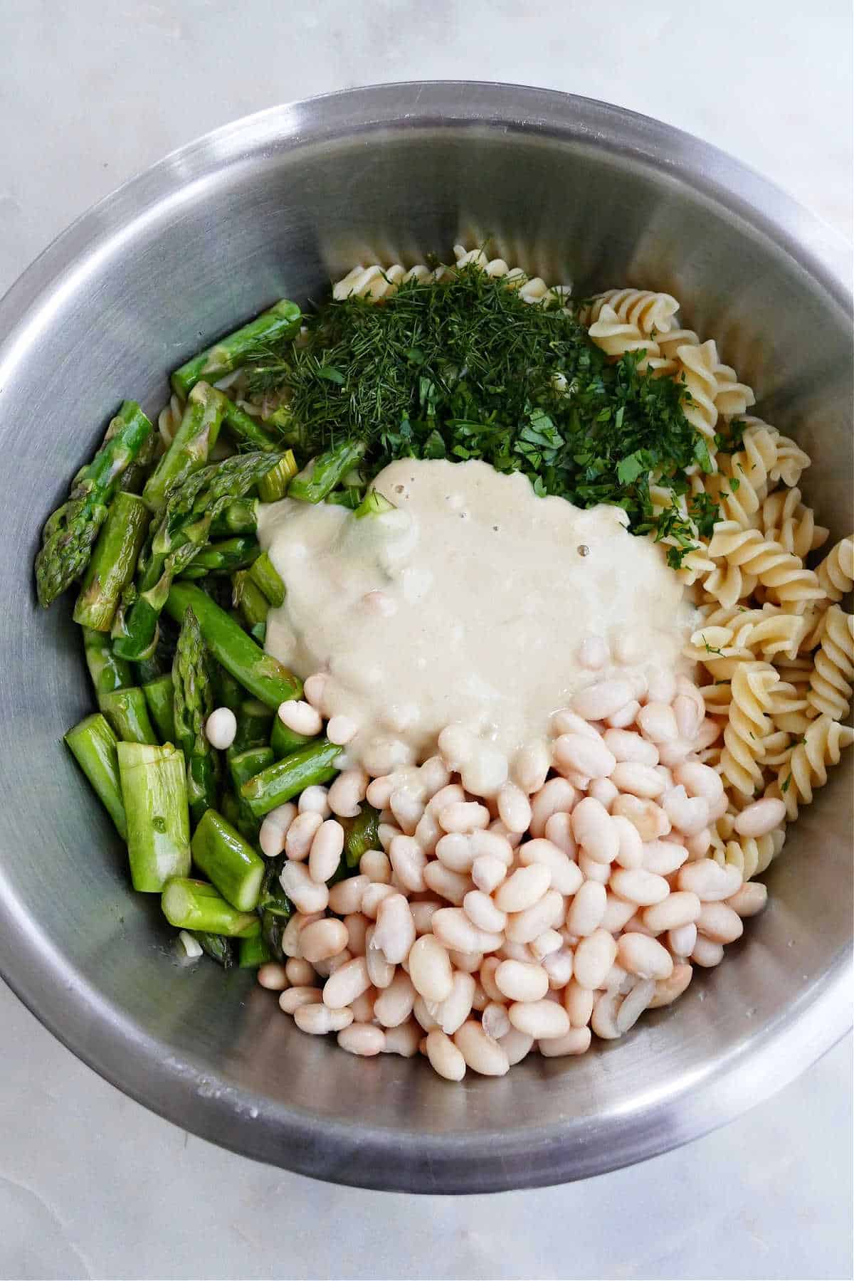 ingredients for asparagus pasta salad and tahini dressing in a bowl on a counter