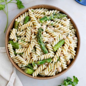 asparagus pasta salad in a bowl next to herbs and toppings on a counter