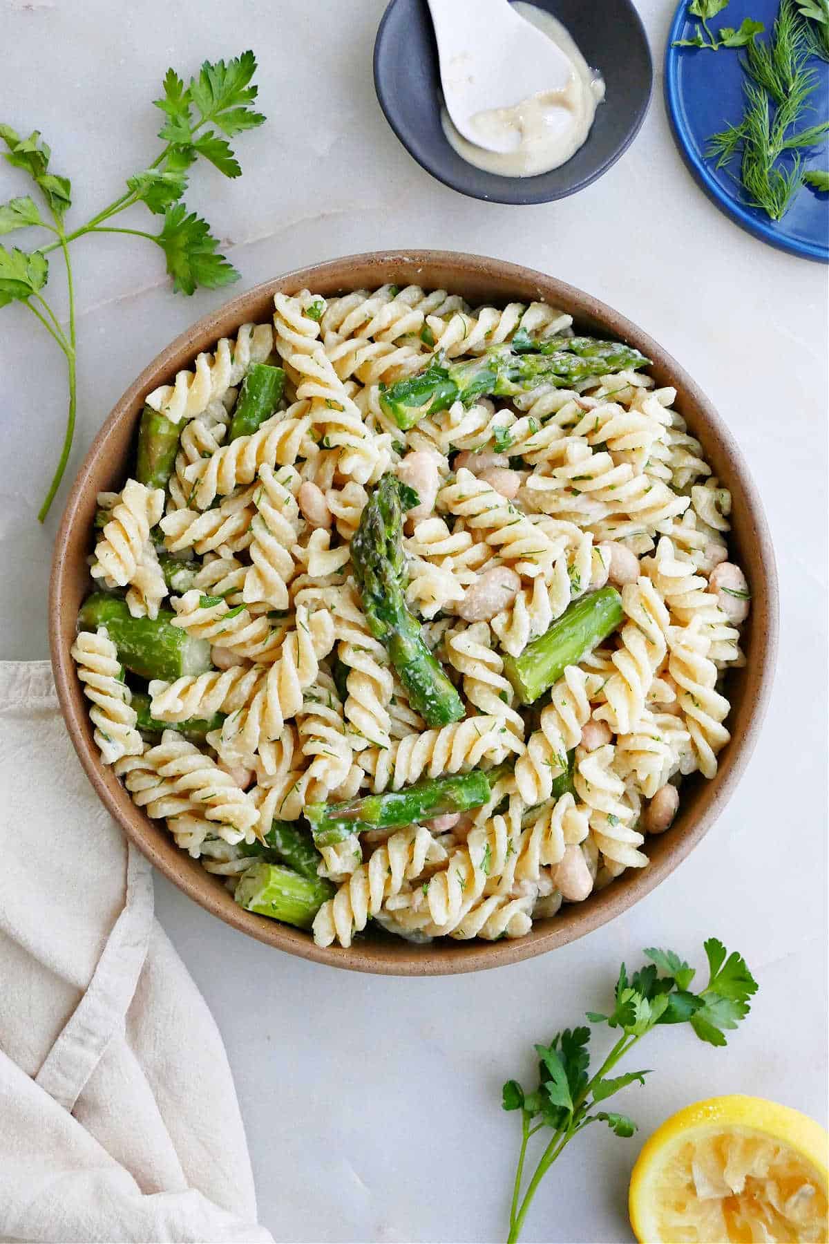 asparagus pasta salad in a bowl next to herbs and toppings on a counter