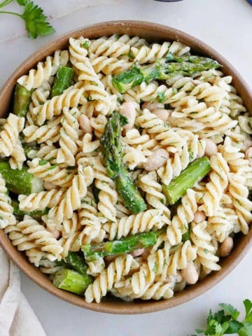 square image of pasta salad with asparagus and fresh herbs in a serving bowl