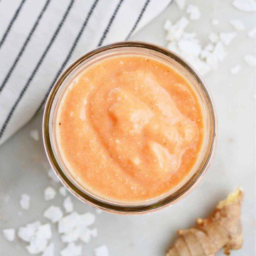 carrot banana smoothie in a glass next to ingredients and a napkin