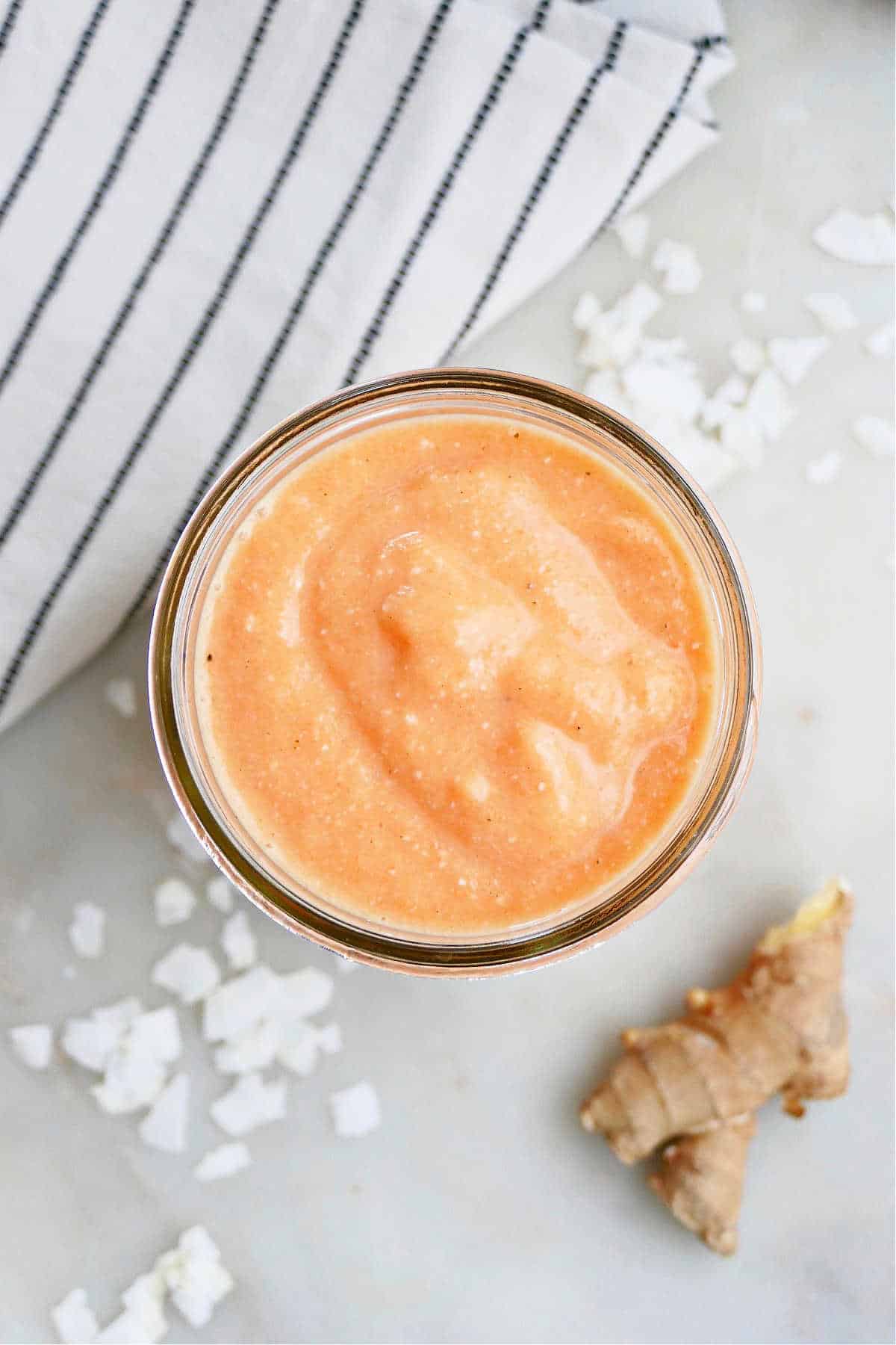 carrot banana smoothie in a glass next to ingredients and a napkin