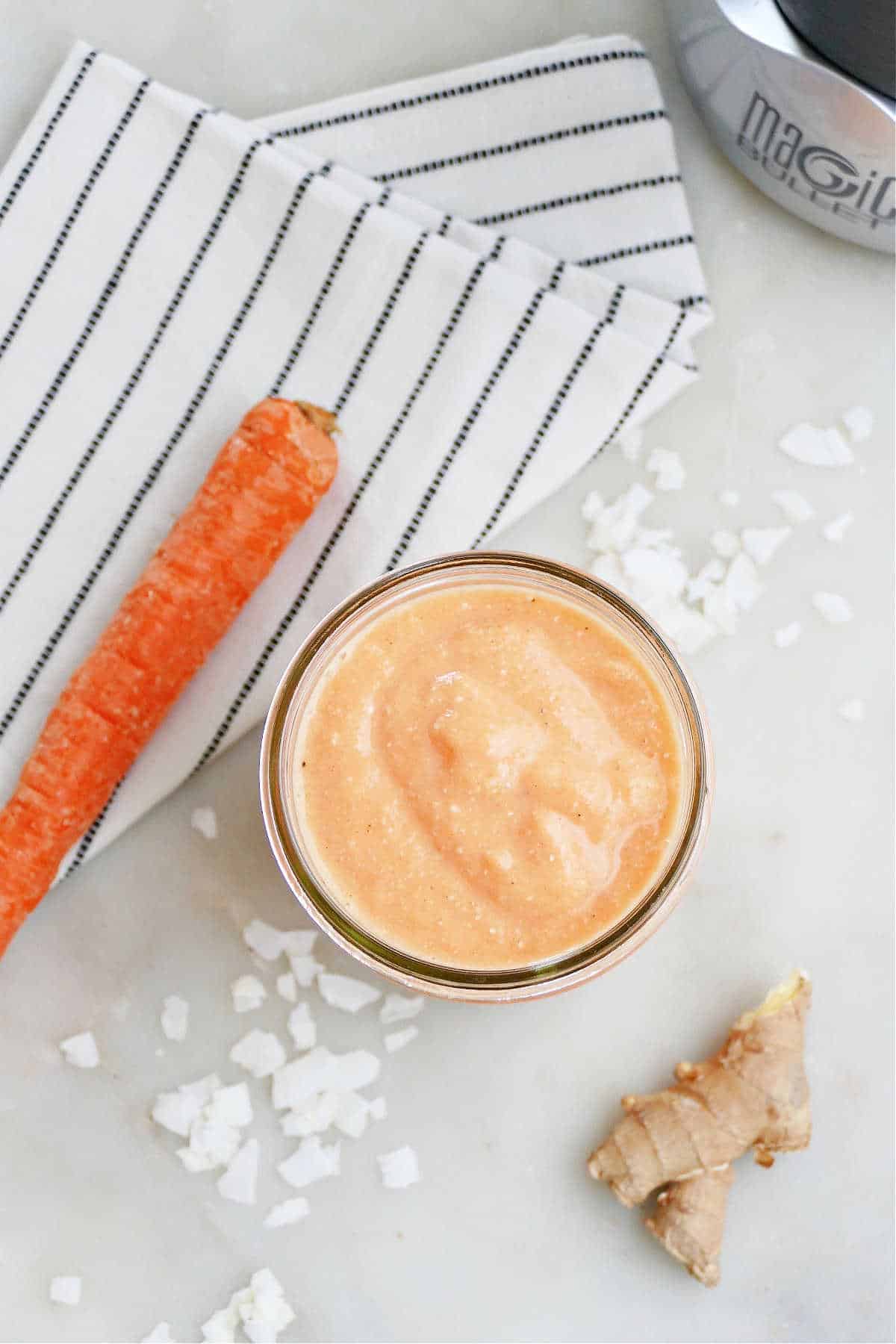 overhead image of carrot smoothie next to ingredients and a striped napkin