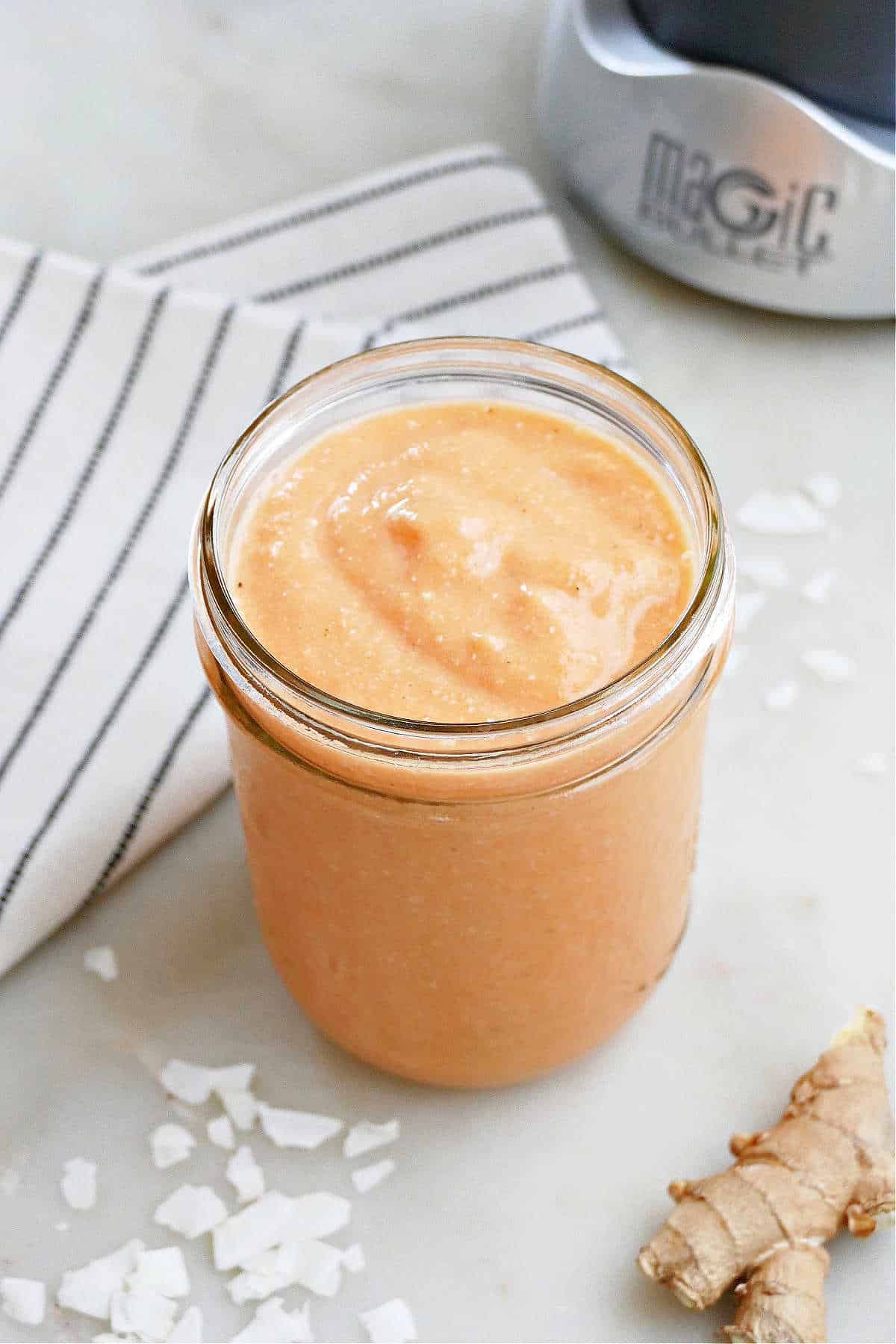 side angle shot of carrot smoothie in a glass next to ingredients