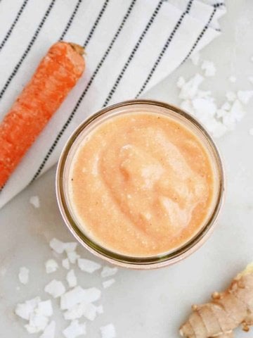 square image of carrot banana smoothie in a glass next to ingredients