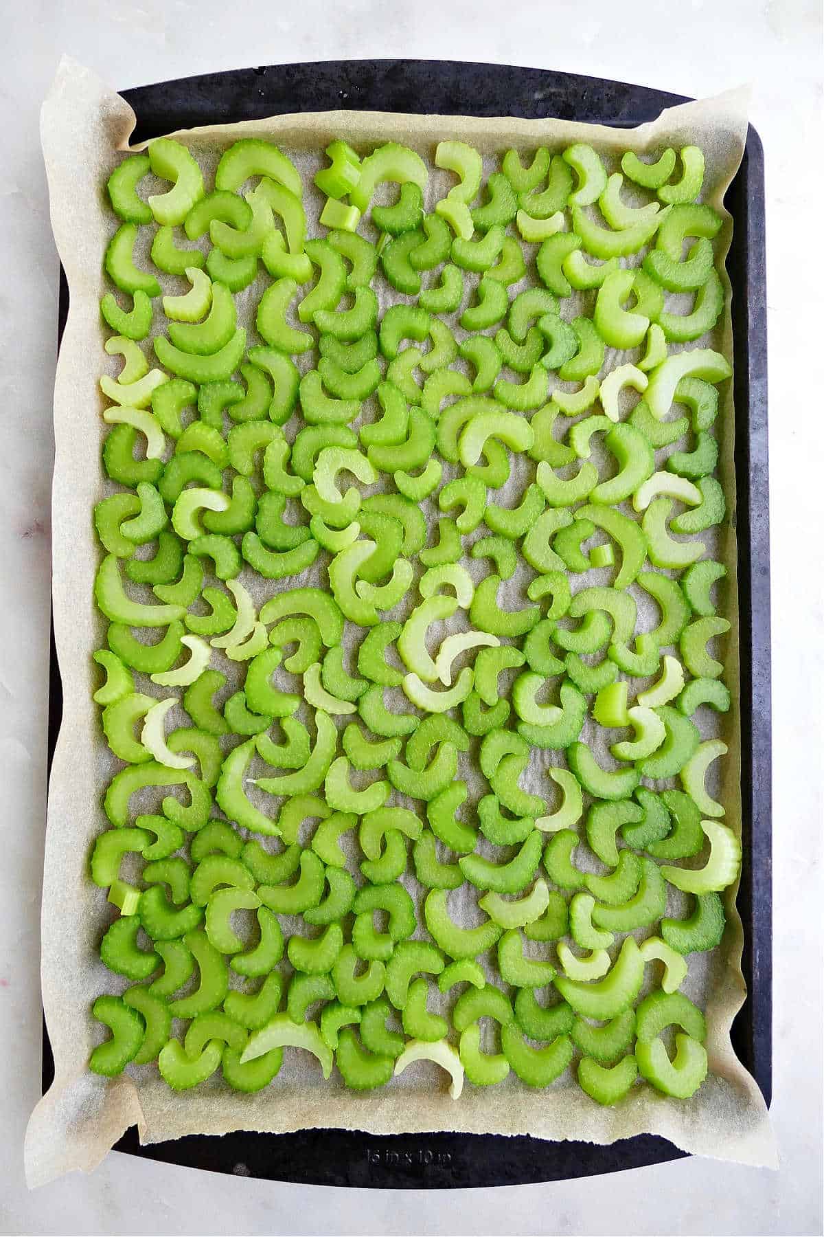 sliced celery spread out on a lined baking sheet for flash freezing