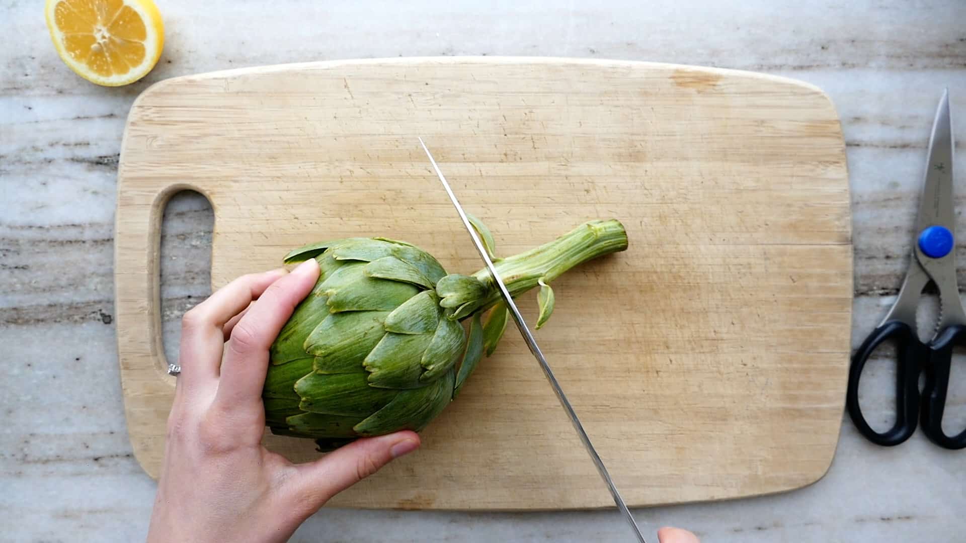 woman slicing off the stem of an artichoke on a cutting board