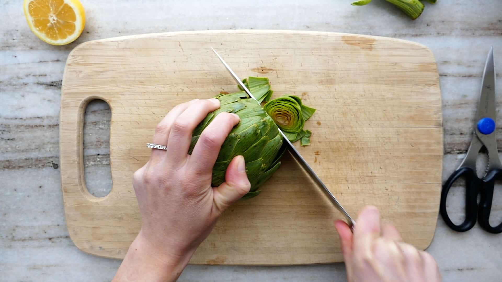 woman slicing off the top of an artichoke over a cutting board