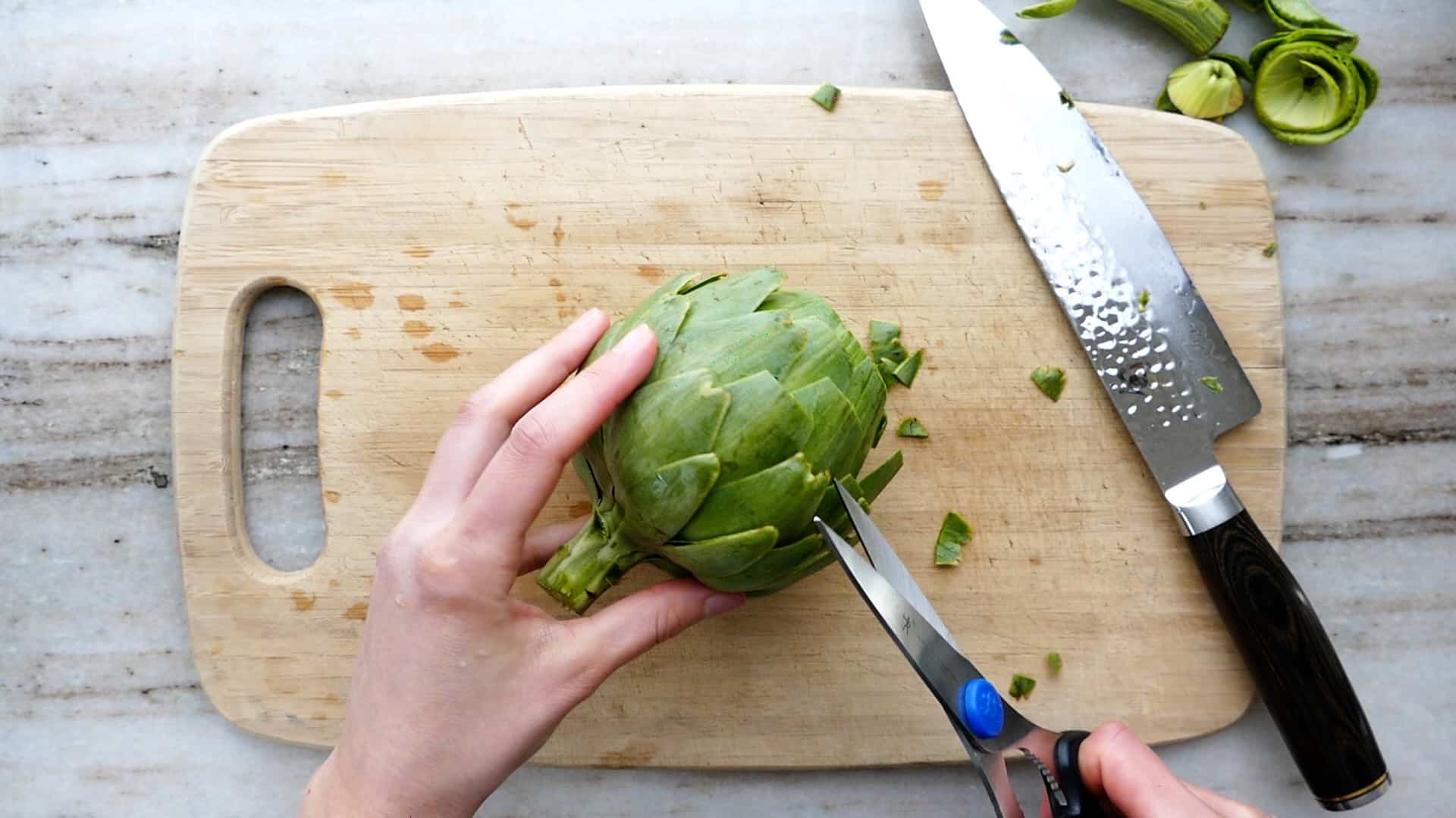 woman snipping artichoke leaves with kitchen scissors over a cutting board