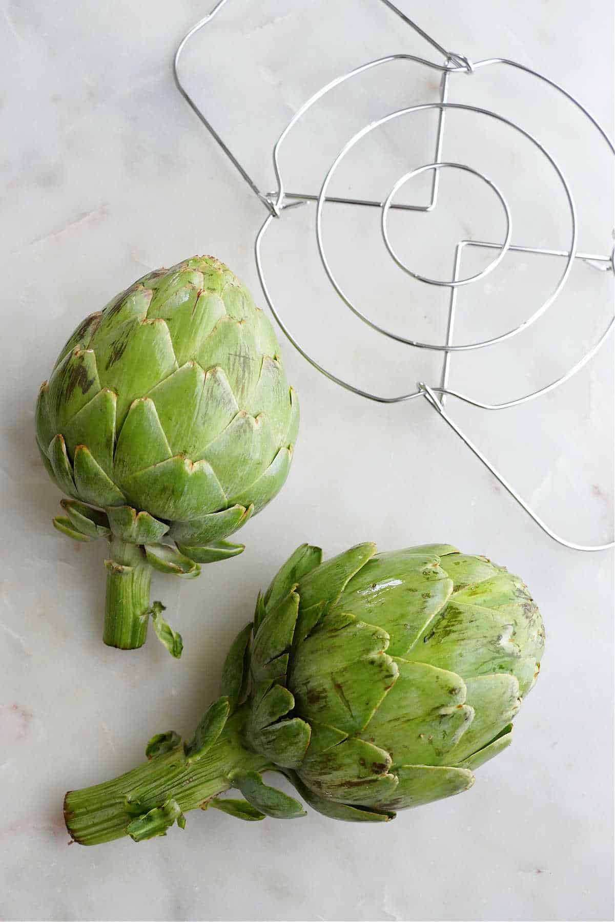 two artichokes next to an instant pot trivet on a counter
