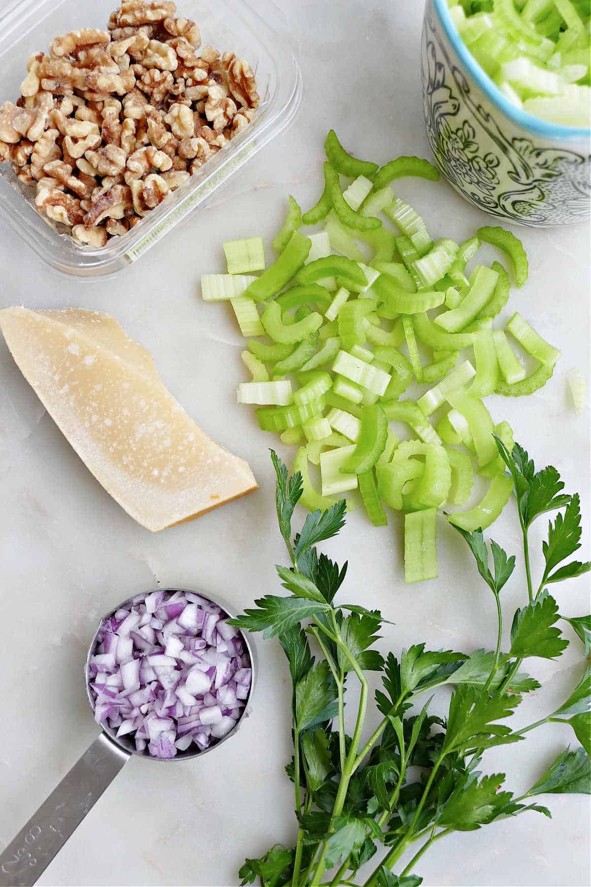 walnuts, parmesan, celery, parsley, and red onion spread out on a counter