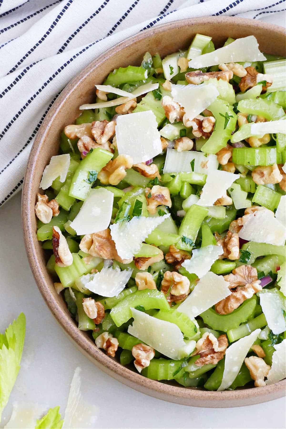 close image of celery, walnut, and parmesan salad in a serving bowl next to napkin