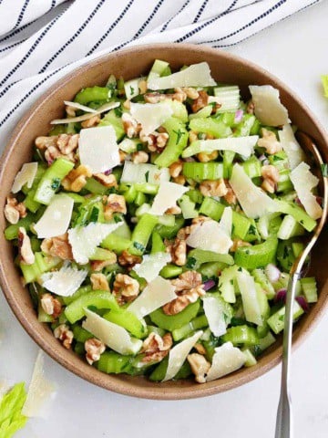 square image of marinated celery salad in a serving bowl next to a striped napkin
