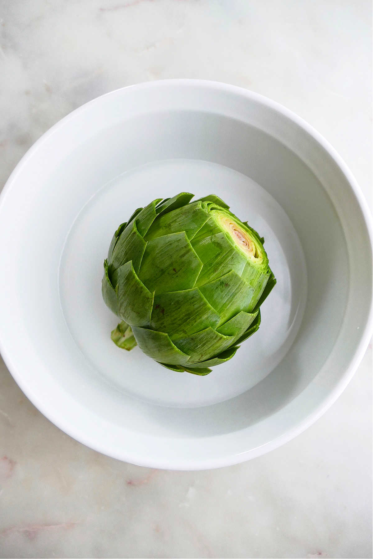 artichoke sitting in a round baking dish with water in the bottom