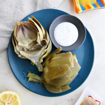 microwave artichoke sliced in half on a serving plate with dipping sauce