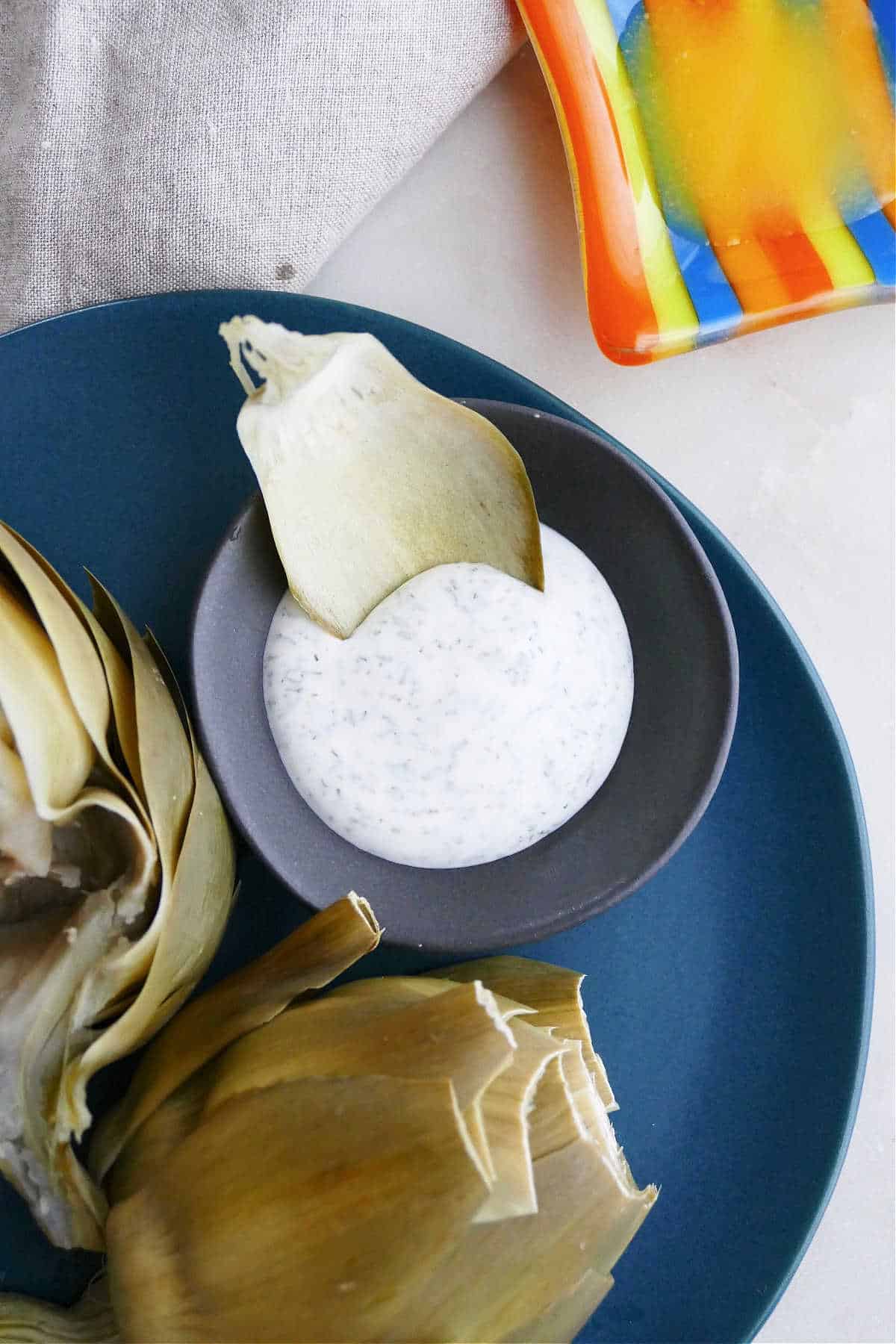 image of an artichoke leaf being dipping into a yogurt sauce on a plate