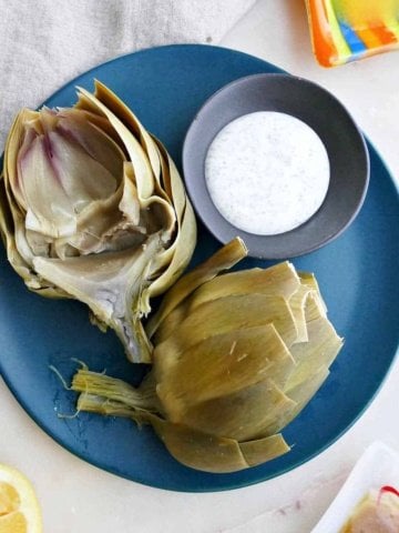 square image of microwave artichoke on a serving dish with dipping sauce