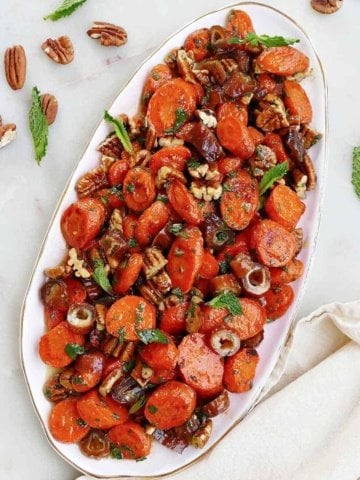square image of spiced carrots and dates on an oval serving dish on a counter